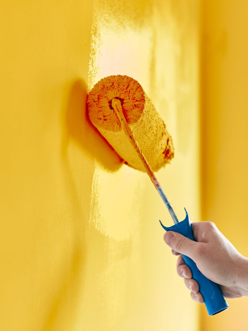 Main tenant un rouleau à peinture à manche bleu appliquant de la peinture jaune sur un mur.