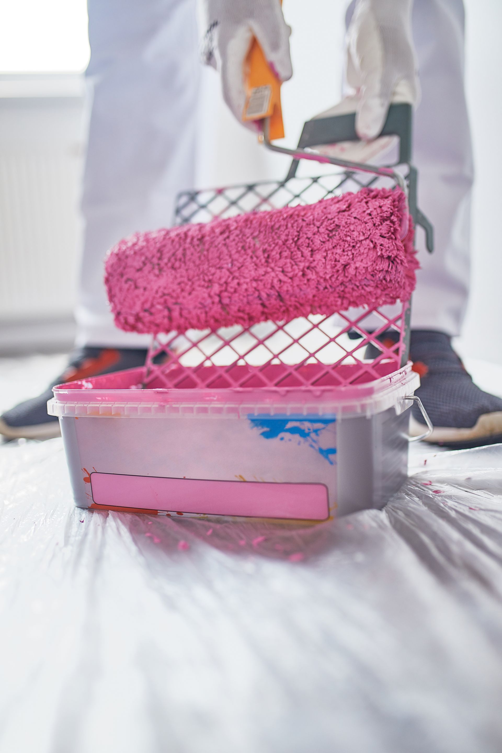 Personne utilisant un rouleau à peinture avec de la peinture rose dans un bac, recouvrant une pièce.