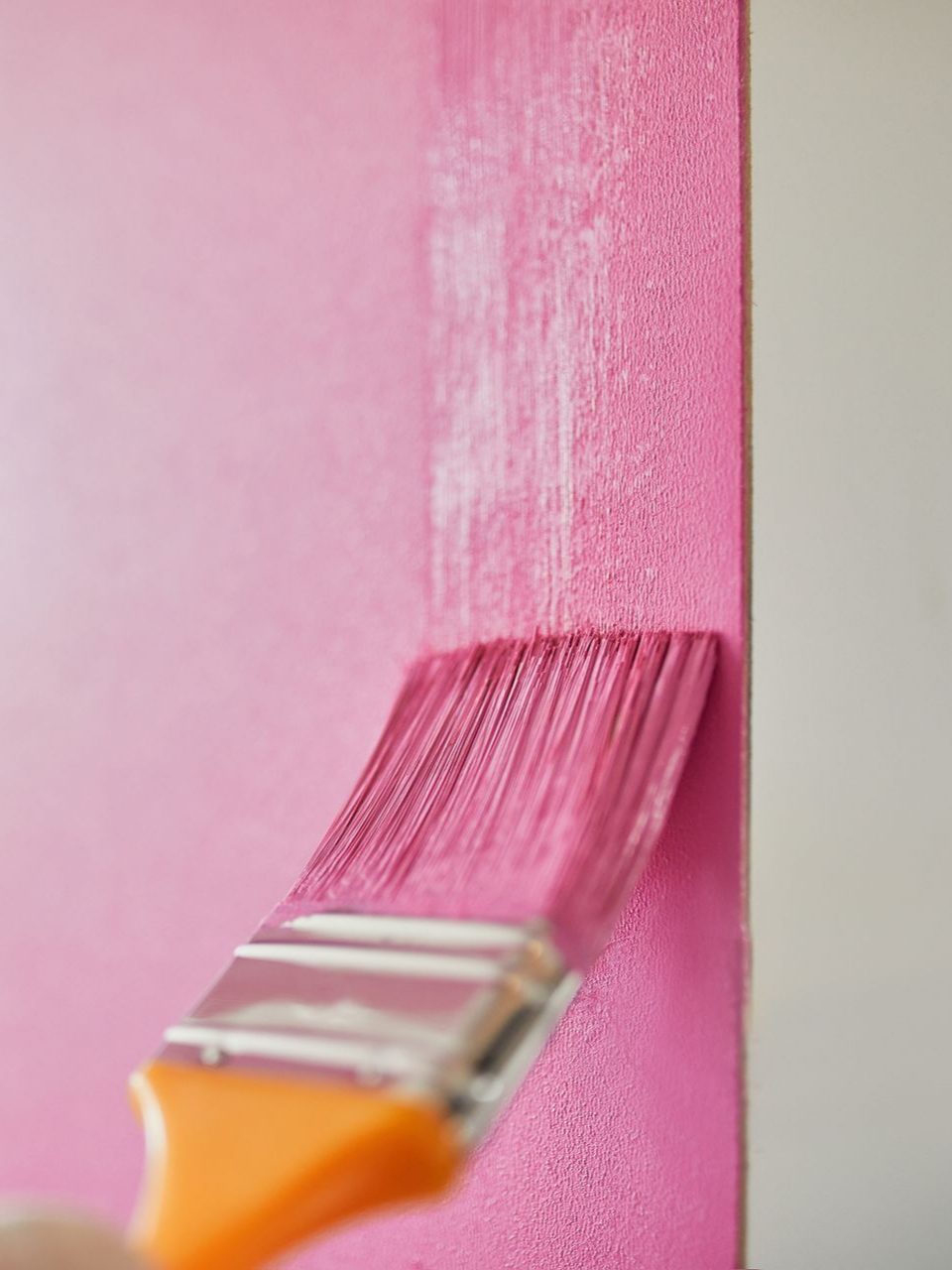 Peinture rose appliquée sur un mur avec un pinceau à manche orange.