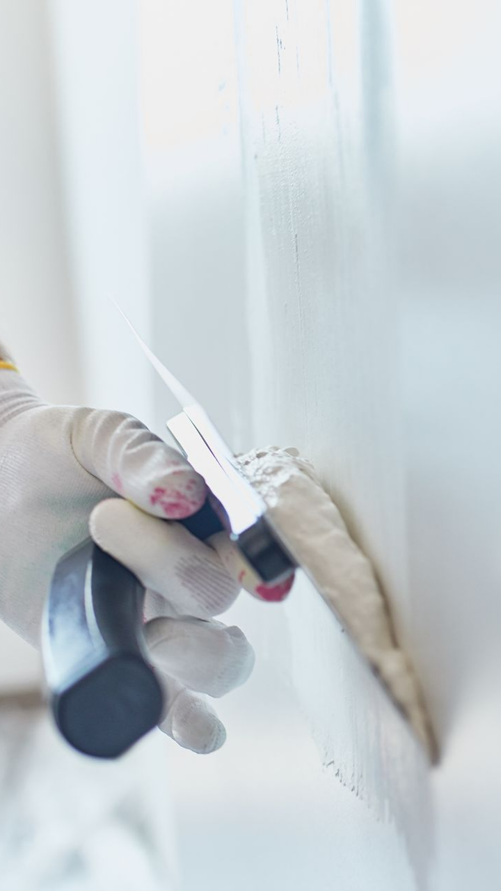 Main gantée utilisant un couteau à mastic pour étaler du mastic blanc sur un mur.