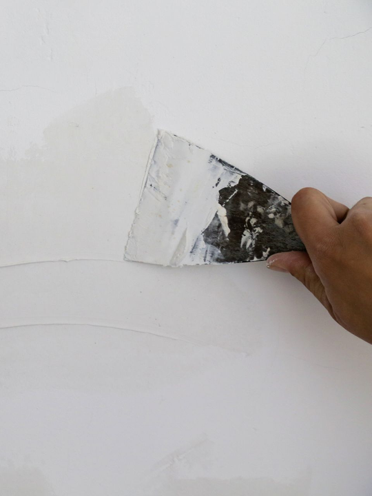 Application manuelle d'un composé blanc sur le mur à l'aide d'un couteau à mastic en métal.