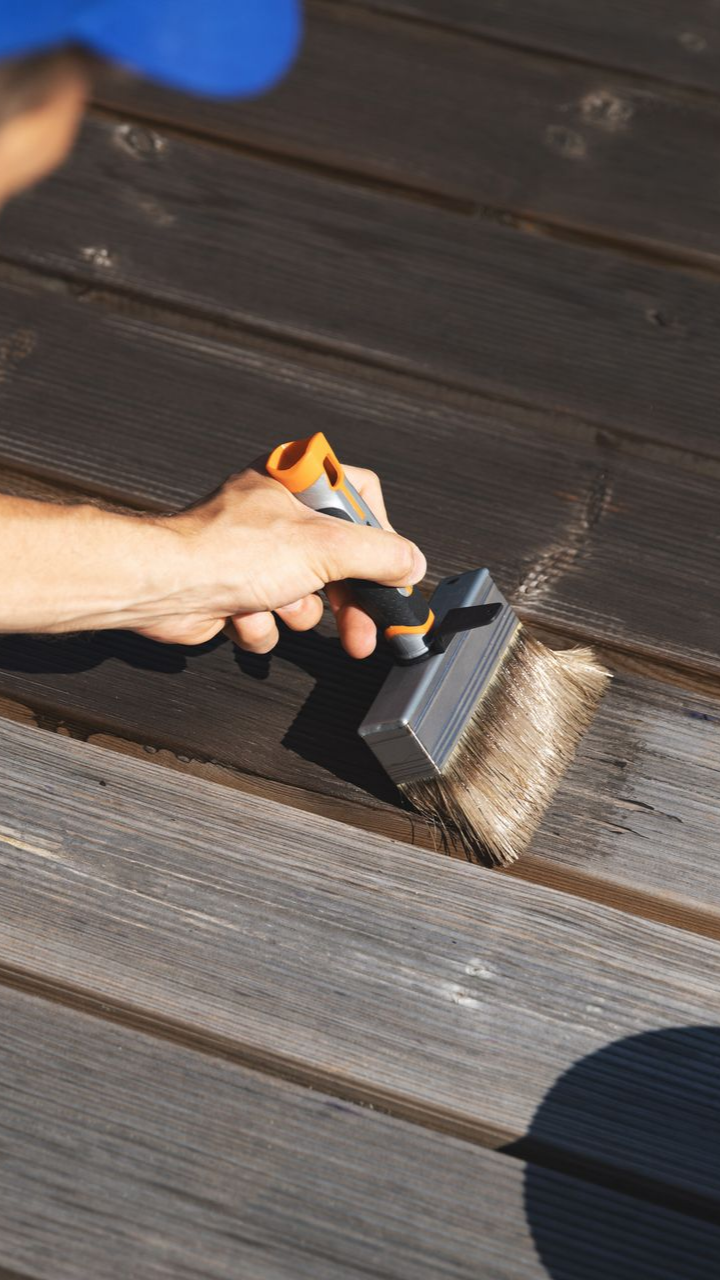 Personne utilisant un pinceau pour appliquer une teinture foncée sur des planches de bois.