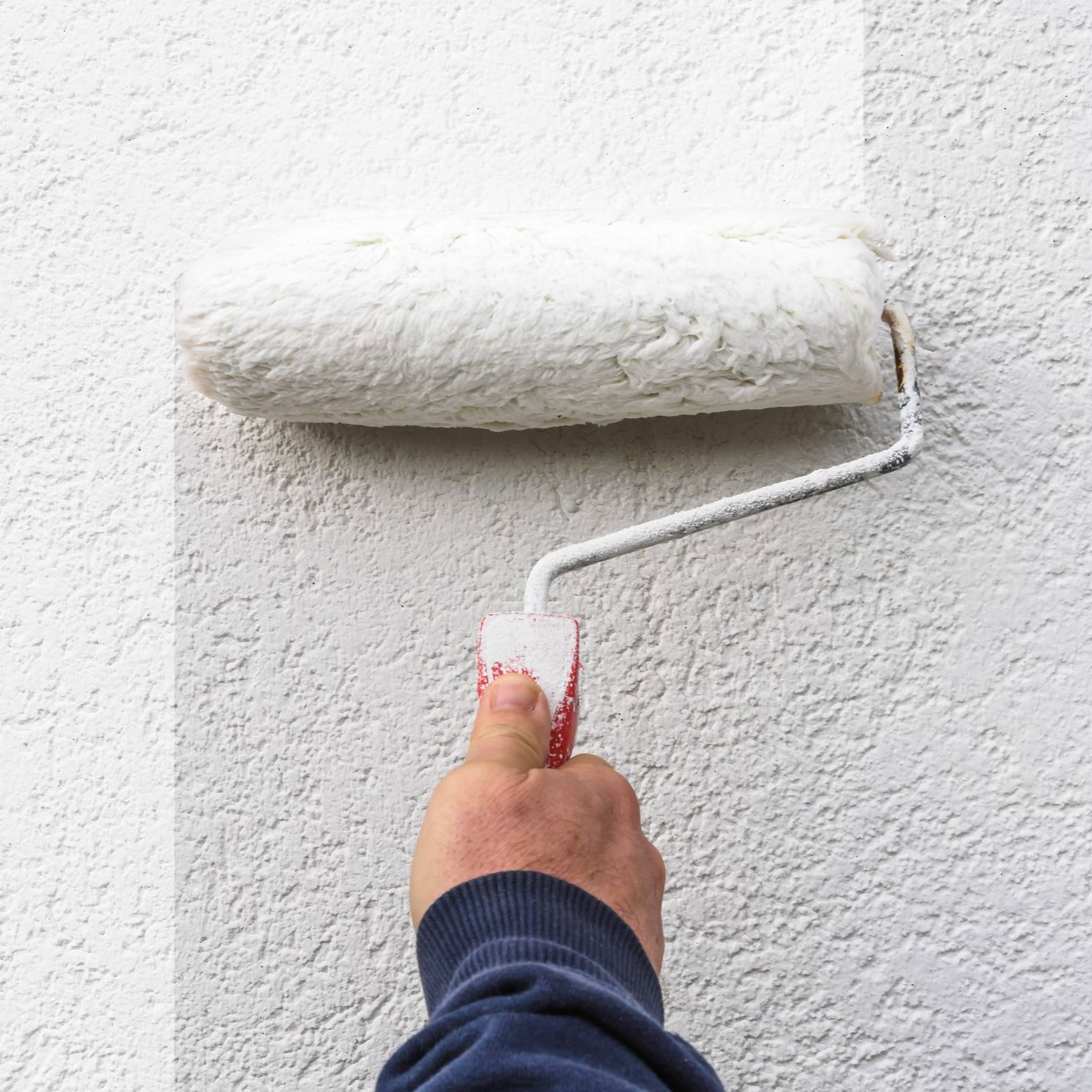 Main tenant un rouleau à peinture appliquant de la peinture blanche sur un mur texturé.