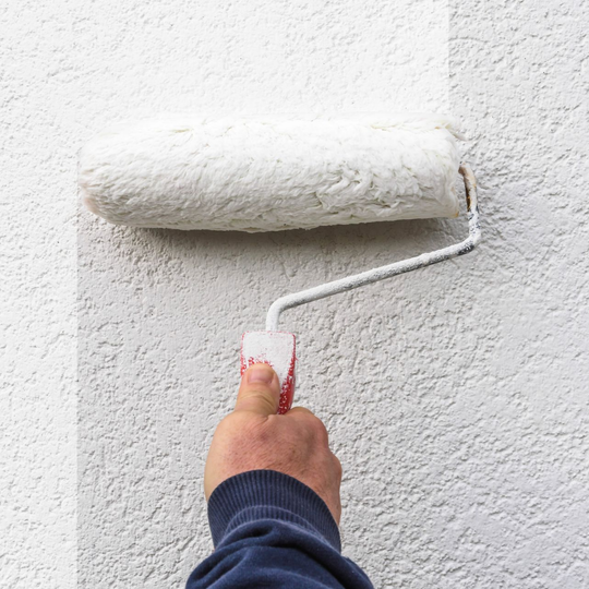 Personne peignant un mur blanc texturé avec un rouleau à peinture.
