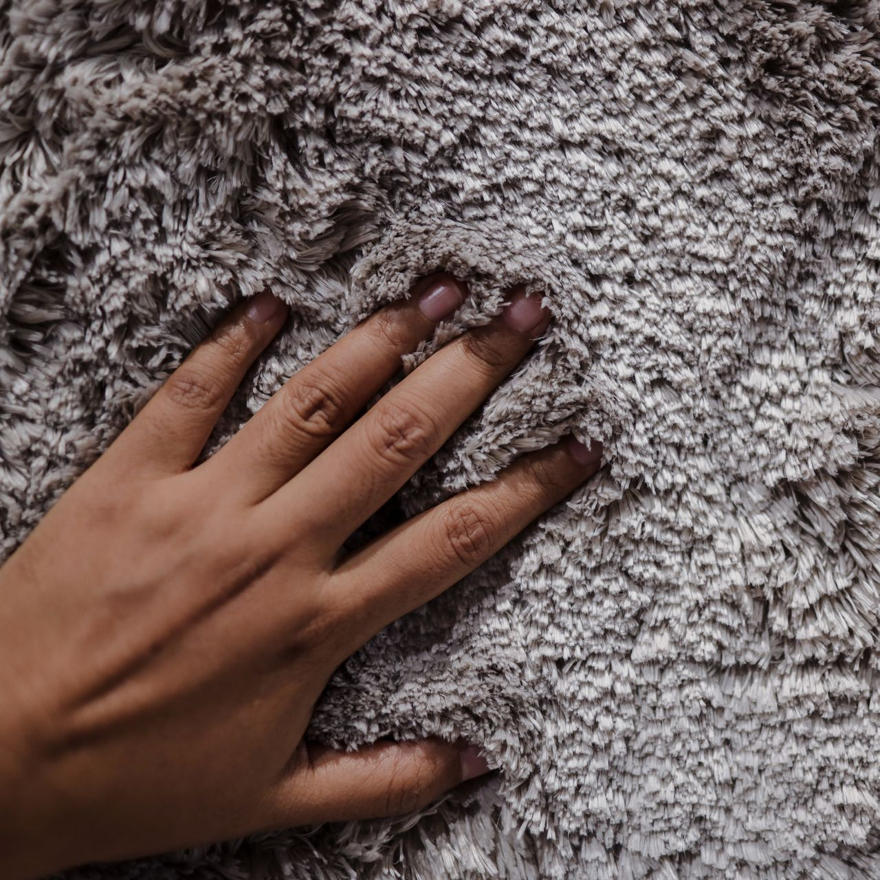 Main touchant un textile doux, gris et moelleux.