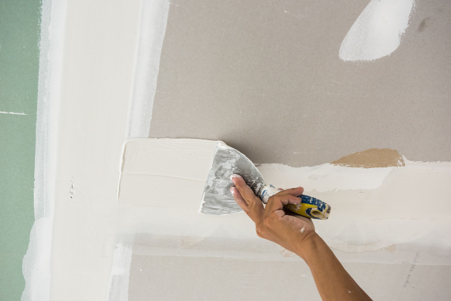 Personne utilisant un couteau à mastic pour appliquer du composé pour cloison sèche sur un mur.