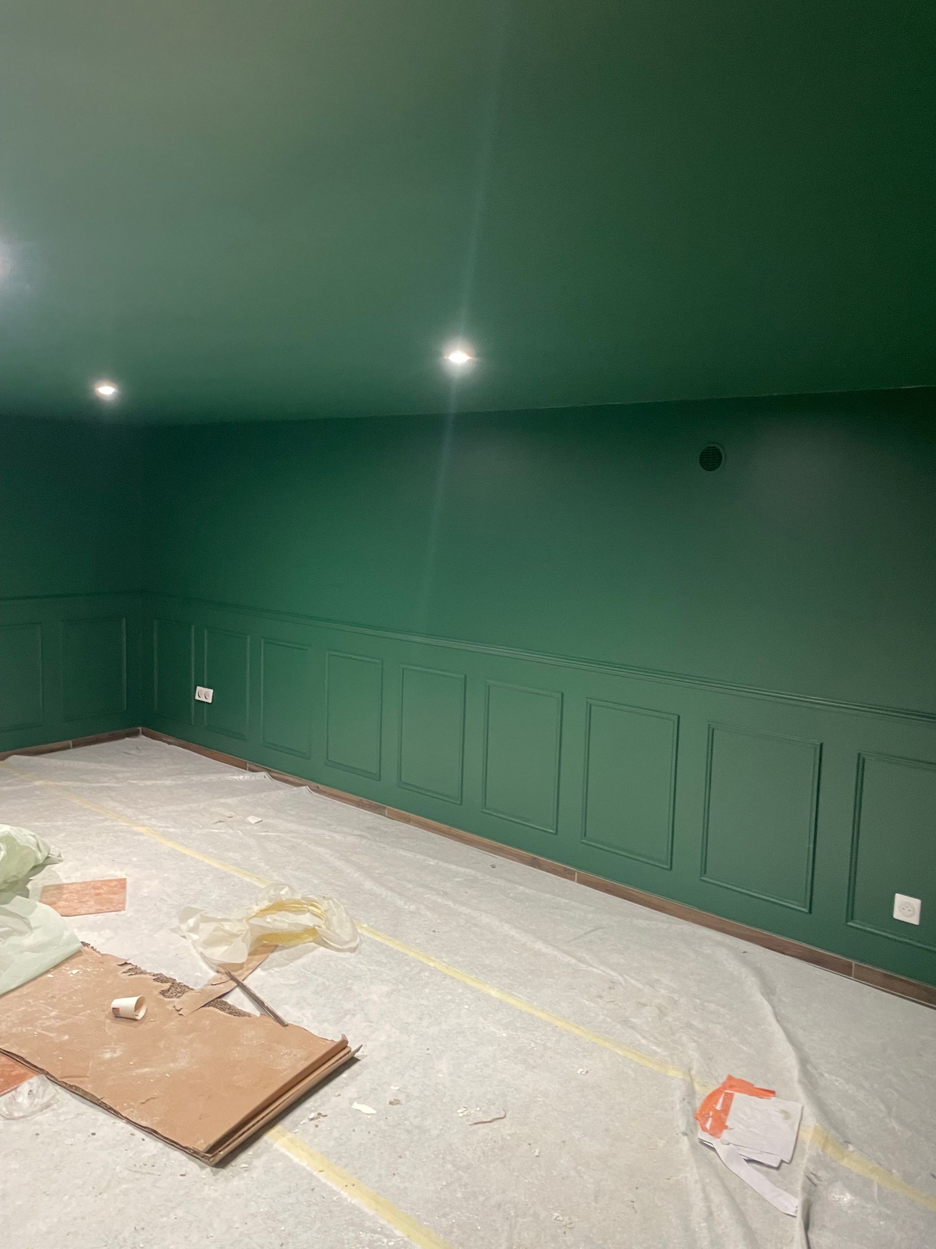 Pièce peinte en vert avec moulures aux murs et deux spots encastrés au plafond. Matériaux de construction au sol.