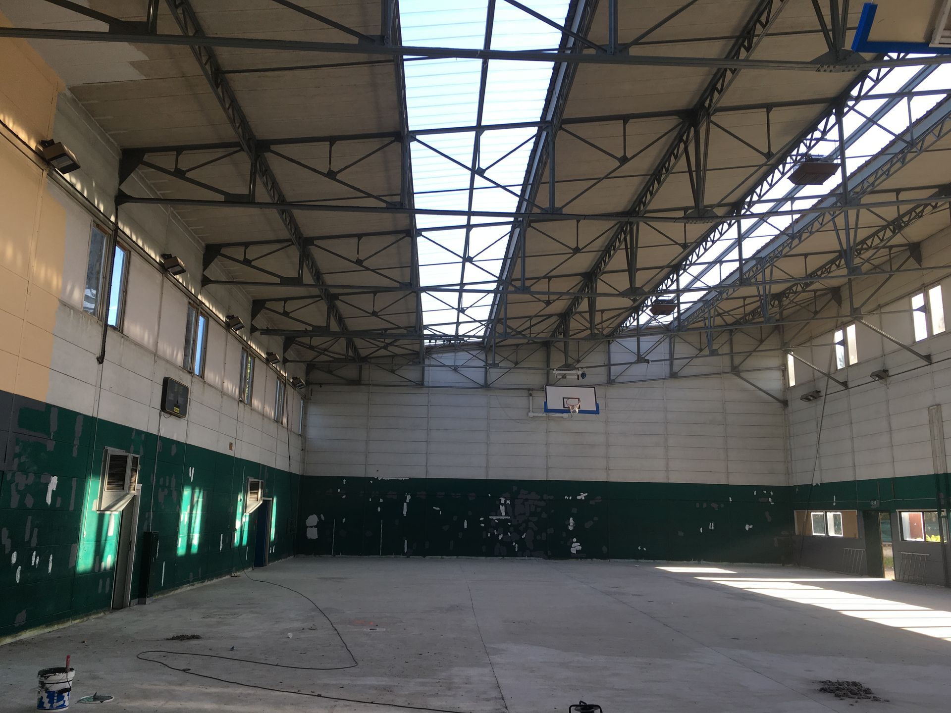 Terrain de sport intérieur vide avec murs végétaux, puits de lumière et poutres métalliques.