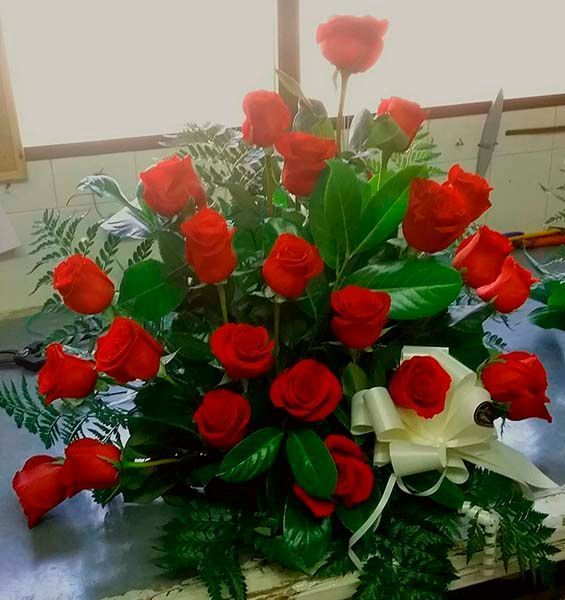 Un ramo de rosas rojas y vegetación sobre una mesa.