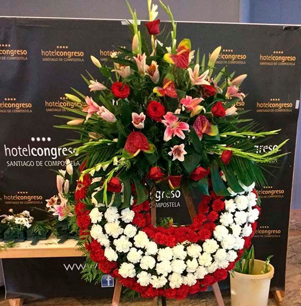 Una corona de flores rojas y blancas frente al cartel del congreso de un hotel.