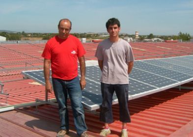 Dos hombres de pie junto a un panel solar en un tejado.