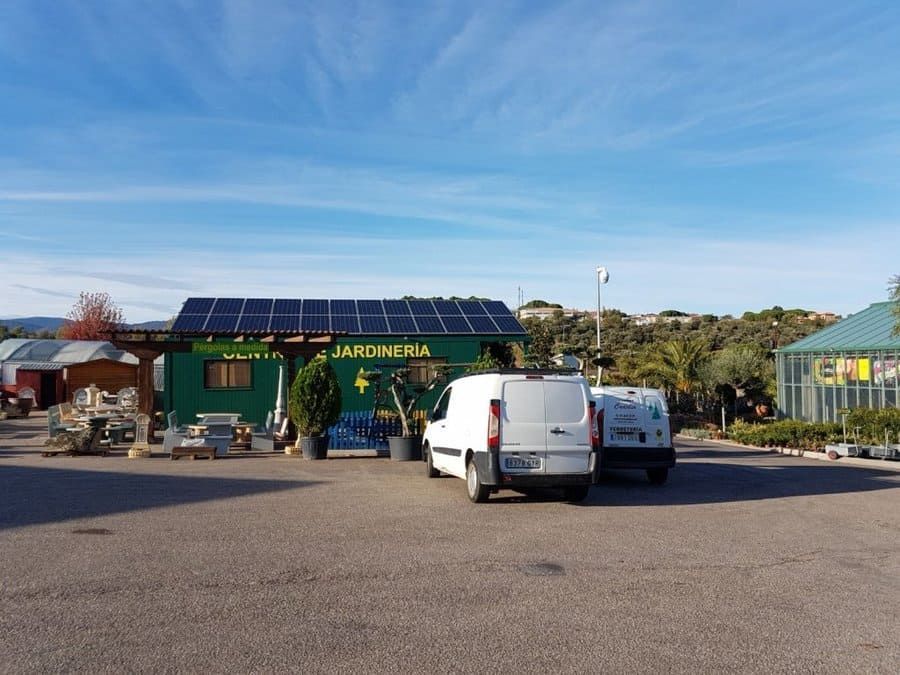 Dos camionetas blancas están estacionadas frente a un edificio verde que dice jardineria