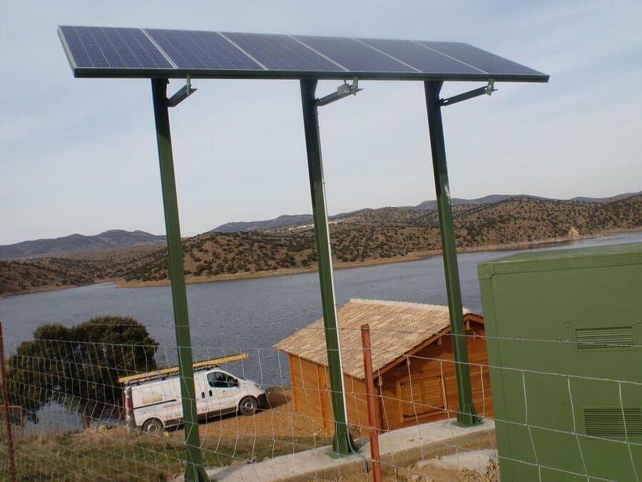 Una camioneta blanca está estacionada frente a un panel solar con vista a un lago.