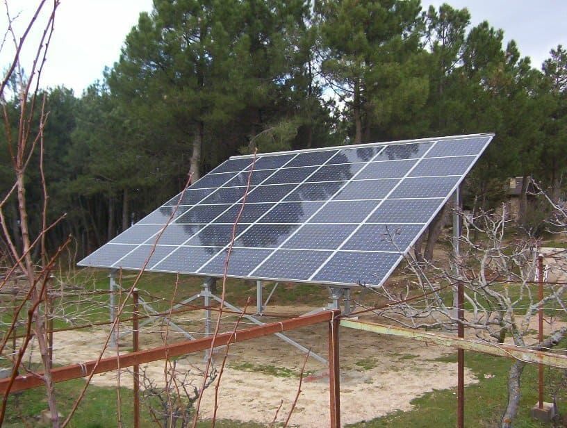 Una fila de paneles solares en un campo con árboles al fondo.