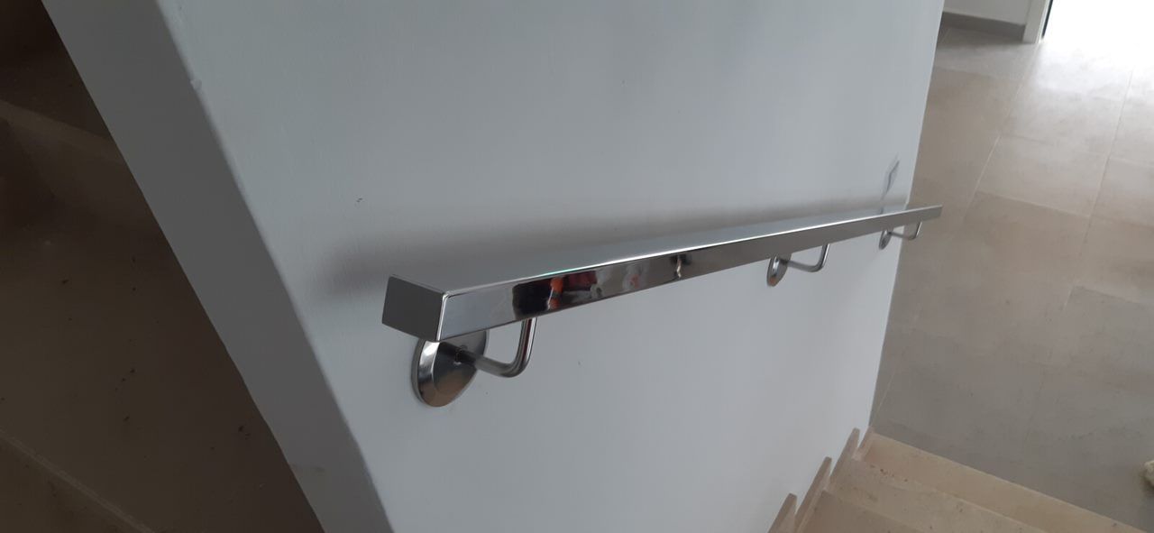 Una barandilla de metal cuelga de una pared blanca al lado de una escalera.