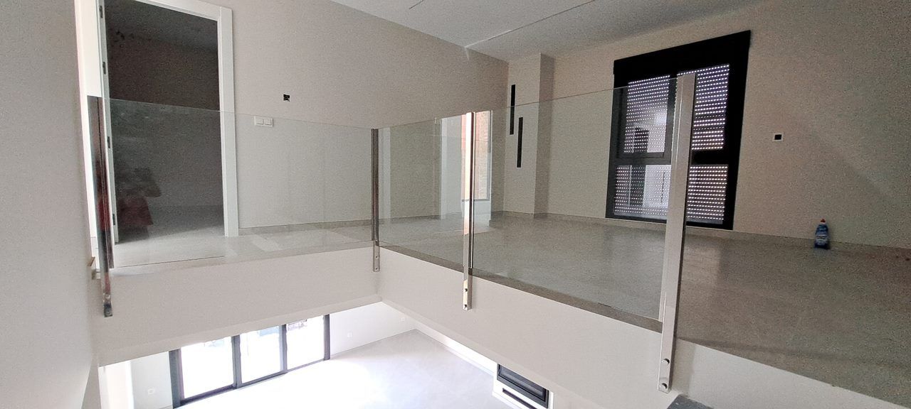 Una habitación vacía con balcón y barandilla de cristal.