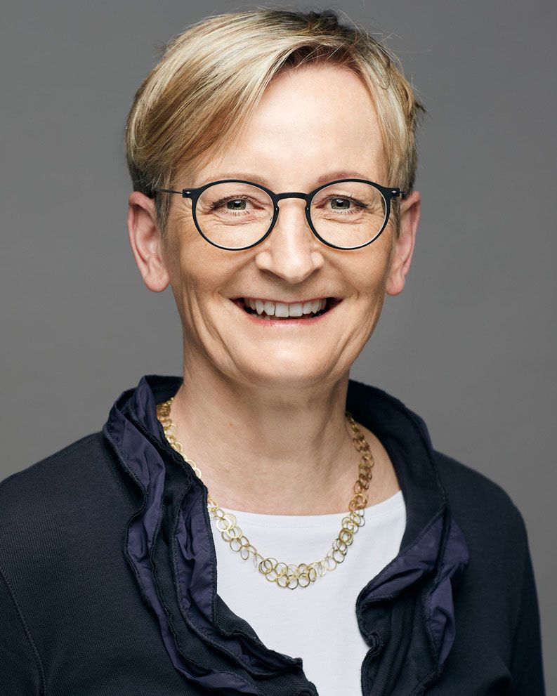 Eine Frau mit Brille und Halskette lächelt in die Kamera.