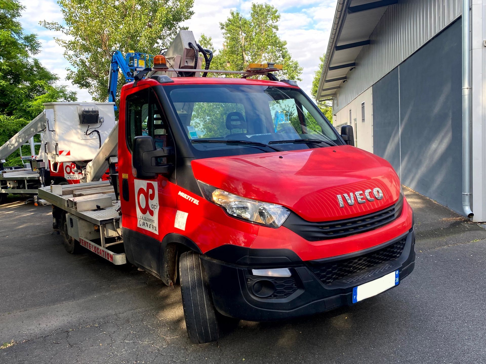 Camion Iveco rouge à plateforme élévatrice stationné près d'un bâtiment.