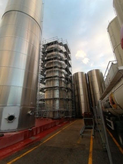 Réservoirs industriels en acier entourés d'échafaudages dans un environnement industriel extérieur.