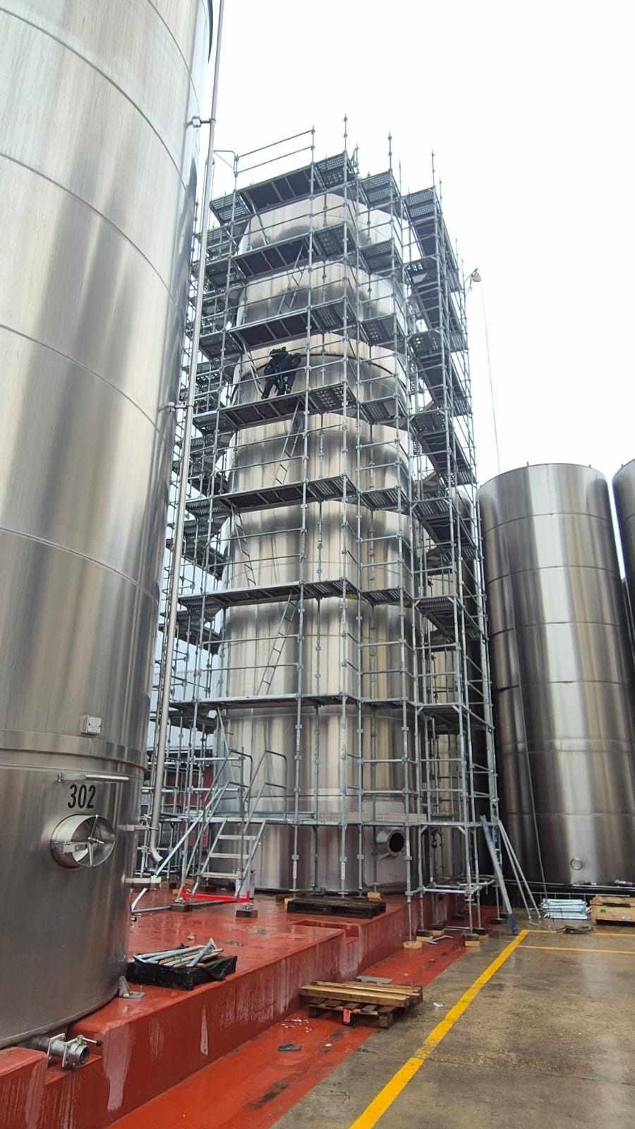 Des échafaudages entourent une grande cuve industrielle cylindrique, d'autres cuves se trouvant à proximité, à l'extérieur.