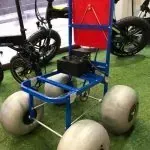 Un carrito azul con ruedas blancas está sentado en el césped al lado de una bicicleta.