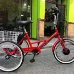 Una bicicleta roja con tres ruedas está estacionada frente a un edificio verde.