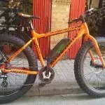 Una bicicleta naranja está estacionada en la acera frente a un edificio rojo.