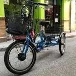 Un triciclo azul con una cesta está aparcado al costado de la carretera.