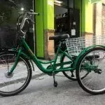 Un triciclo verde está estacionado en la acera frente a un edificio.