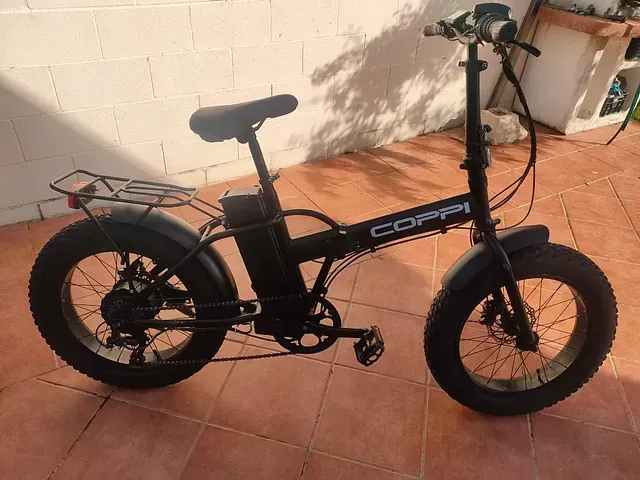 Una bicicleta negra con neumáticos grandes está estacionada en un piso de baldosas.