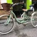 Una bicicleta verde con una cesta está estacionada al costado de la carretera.
