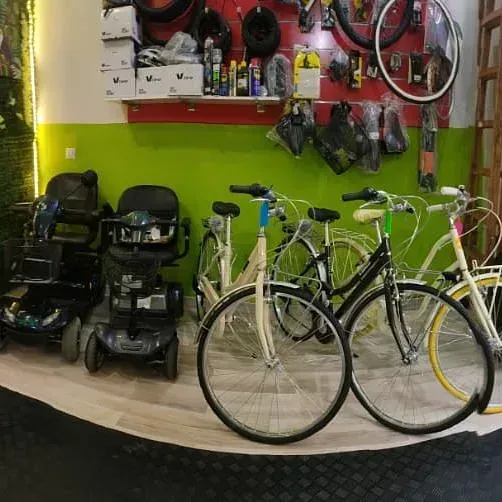 Una fila de bicicletas están estacionadas en una habitación al lado de un scooter de movilidad.