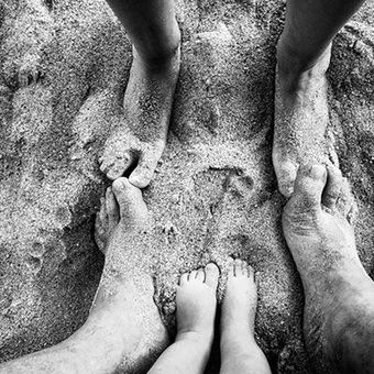 Una fotografía en blanco y negro de los pies de una familia en la arena.