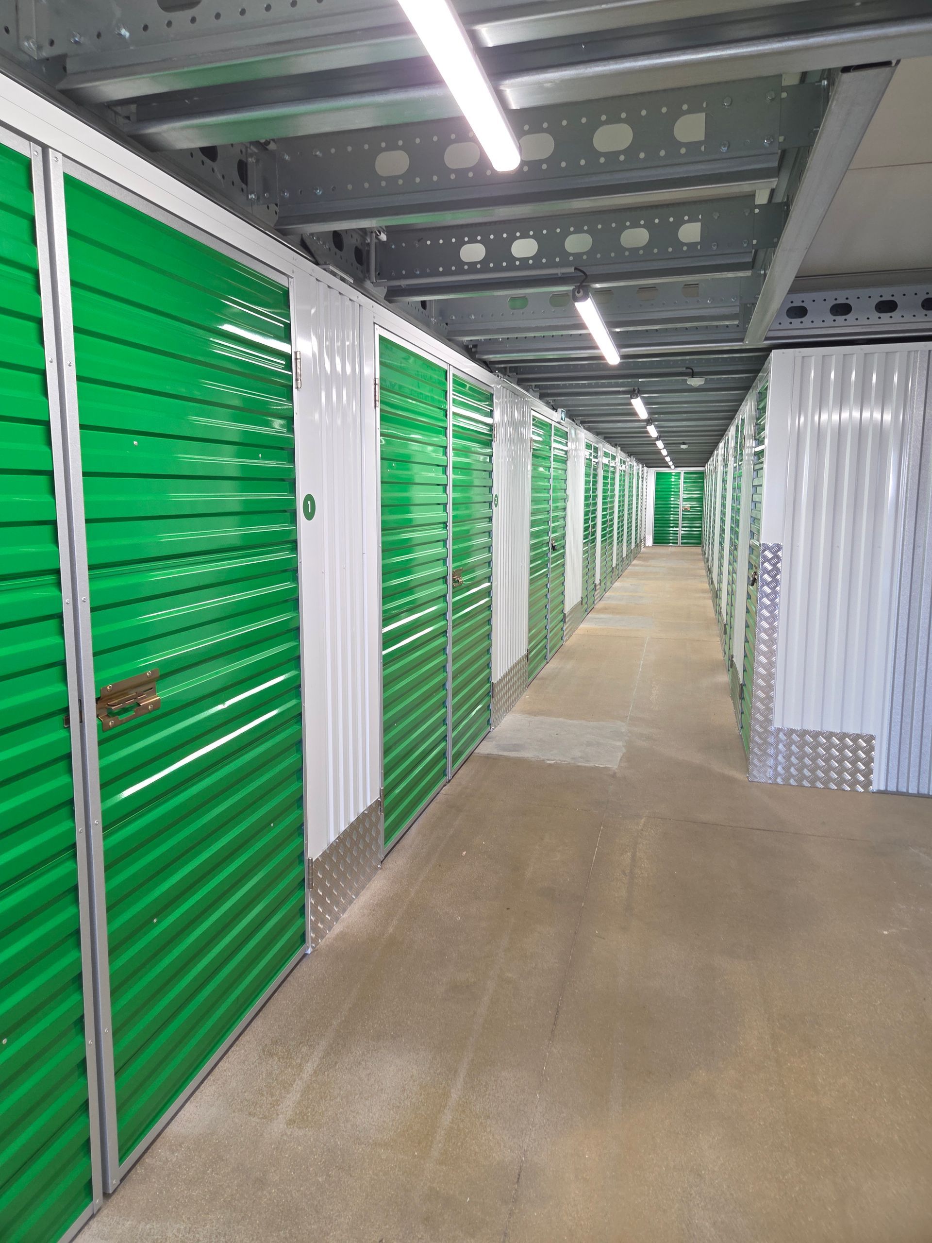 Des box de stockage aux portes turquoise dans un couloir ; des vélos et du matériel sont entreposés dans un box ouvert.