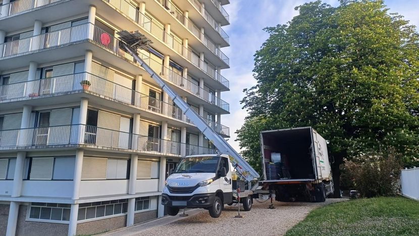 Des ouvriers chargent des débris dans un camion à côté d'un immeuble d'appartements et d'une allée bordée d'arbres