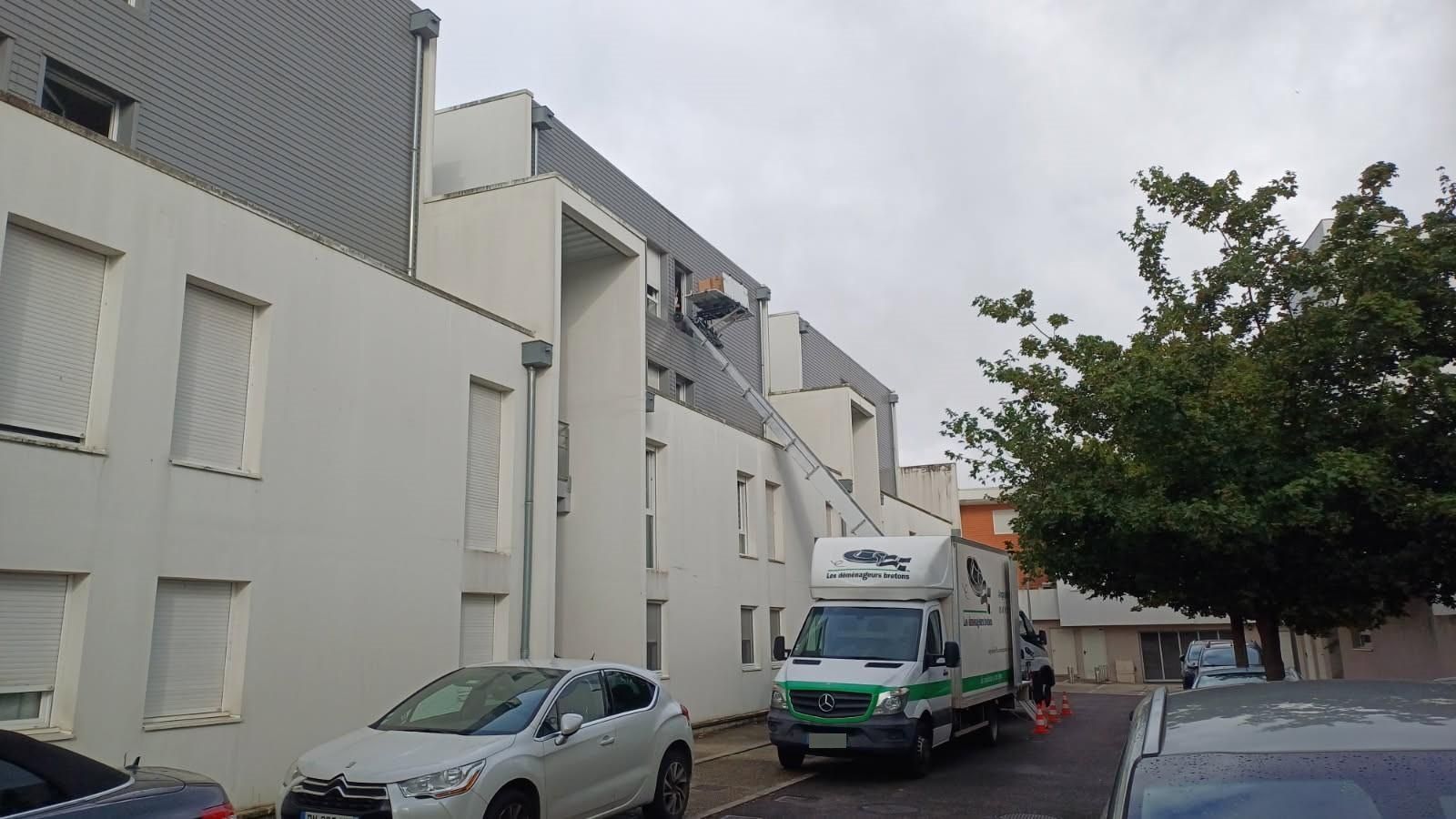 Voitures garées dans une rue résidentielle étroite bordée d'immeubles d'appartements blancs sous un ciel nuageux