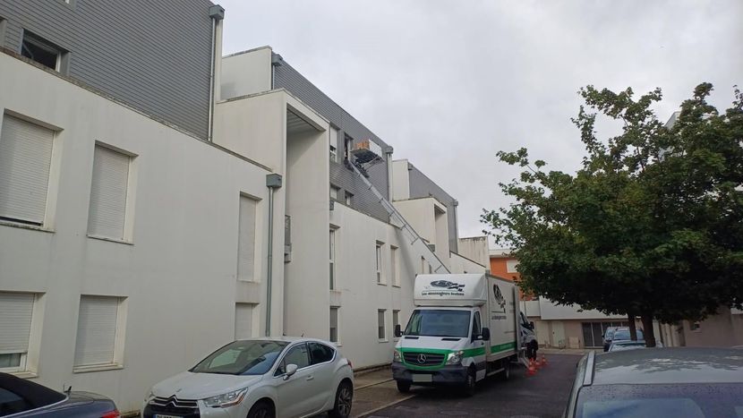 Rue résidentielle étroite avec des voitures garées, des bâtiments blancs et un camion de livraison vert sous un ciel couvert