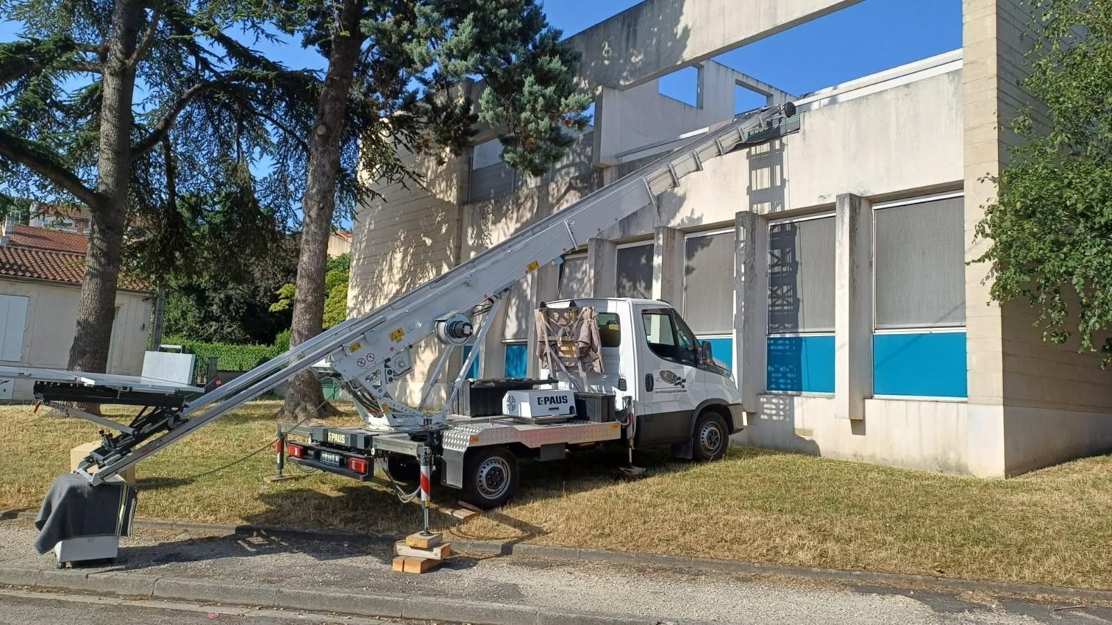 Camion utilitaire à flèche déployée stationné à côté d'un bâtiment, travaillant près des fenêtres supérieures et des moulures bleues.