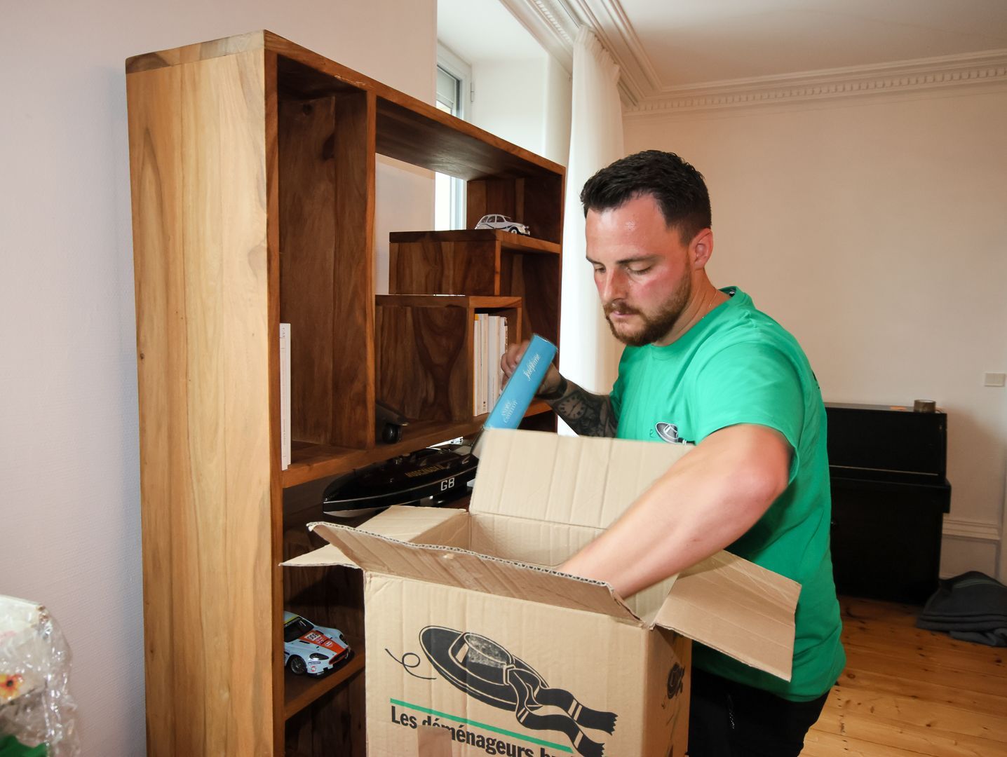 Une personne scotche un carton lors d'un déménagement, avec des cartons empilés en arrière-plan.