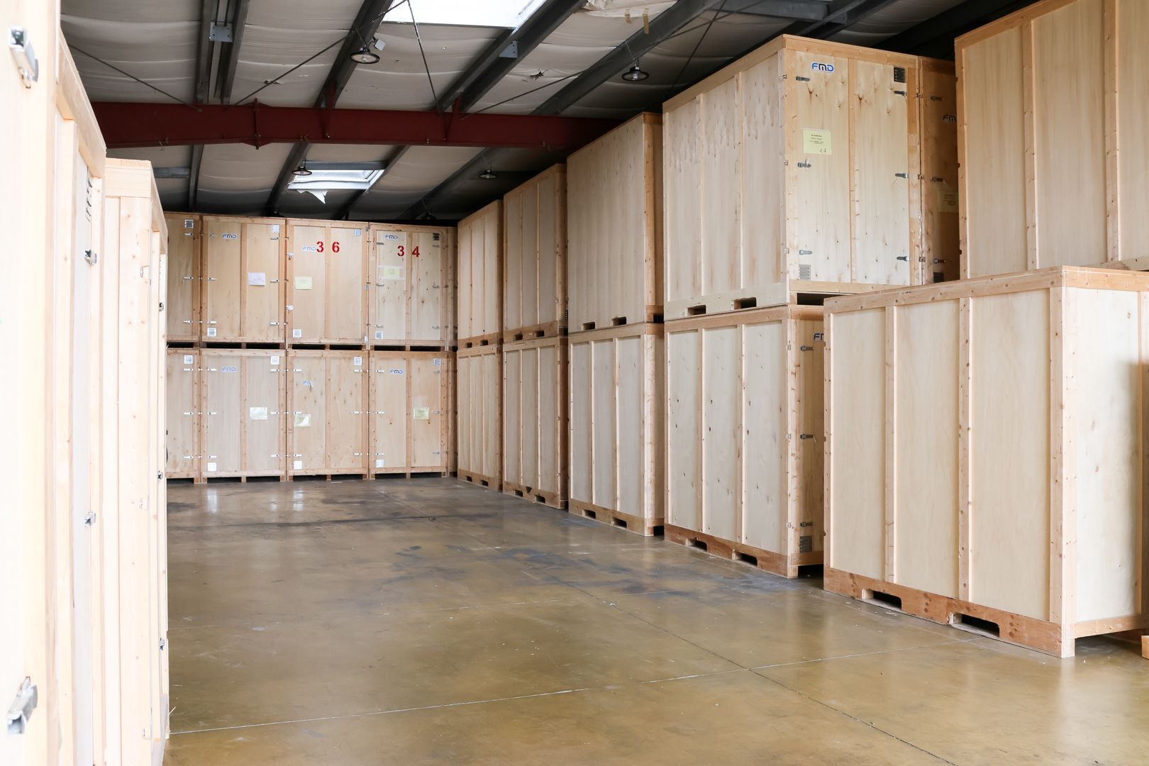 Des box de stockage avec portes sectionnelles rouges dans un couloir intérieur propre, avec des chaises et des cartons empilés près d'un box.