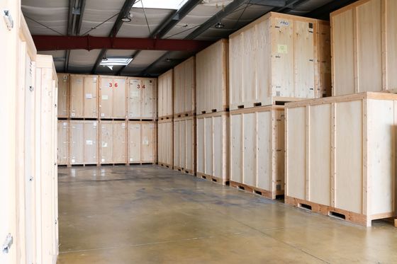 Des box de stockage avec portes sectionnelles rouges dans un couloir intérieur propre, avec des chaises et des cartons empilés près d'un box.