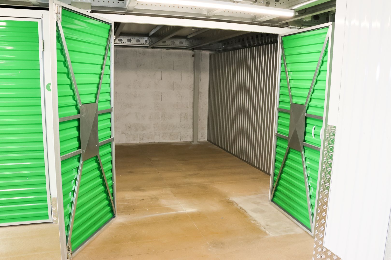 Entrepôt bleu ouvert avec des cartons empilés à l'intérieur, adossés à un mur de briques grises.