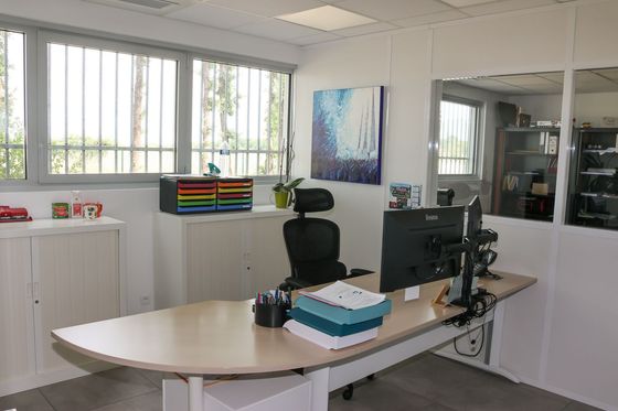 Un espace de travail de bureau encombré, avec des bureaux, des écrans et des chaises emballés dans du plastique, dans une pièce lumineuse