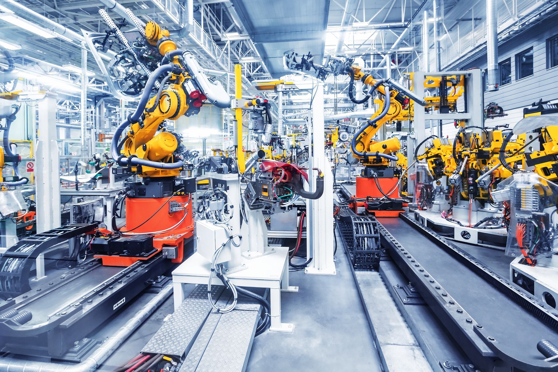 Ligne de production automatisée avec des bras robotisés orange assemblant des pièces dans un atelier industriel lumineux