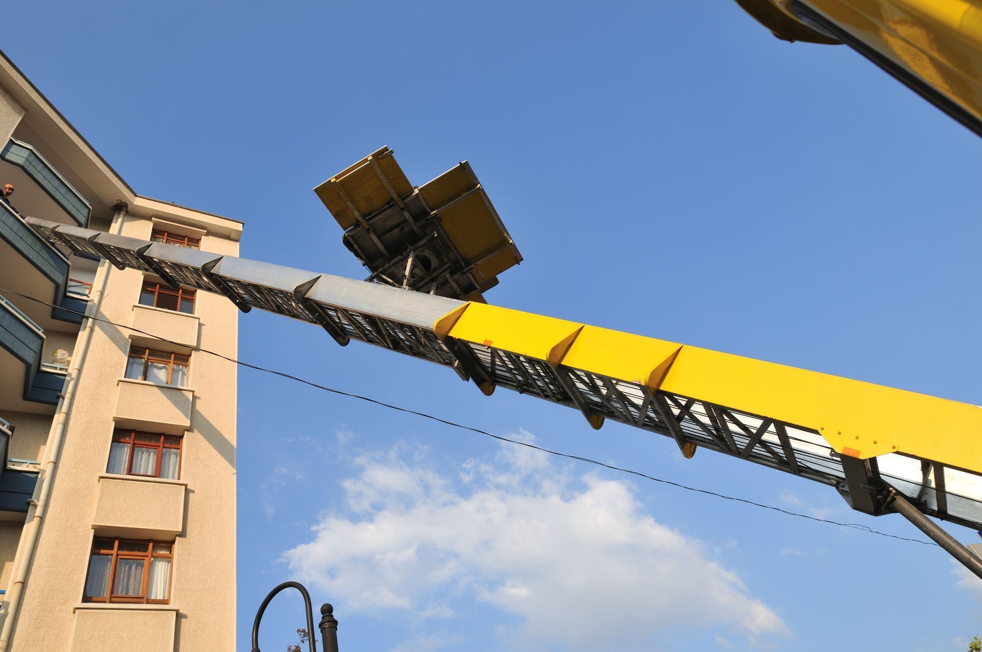 Une grue de chantier soulève des matériaux à côté d'un immeuble d'appartements sous un ciel bleu