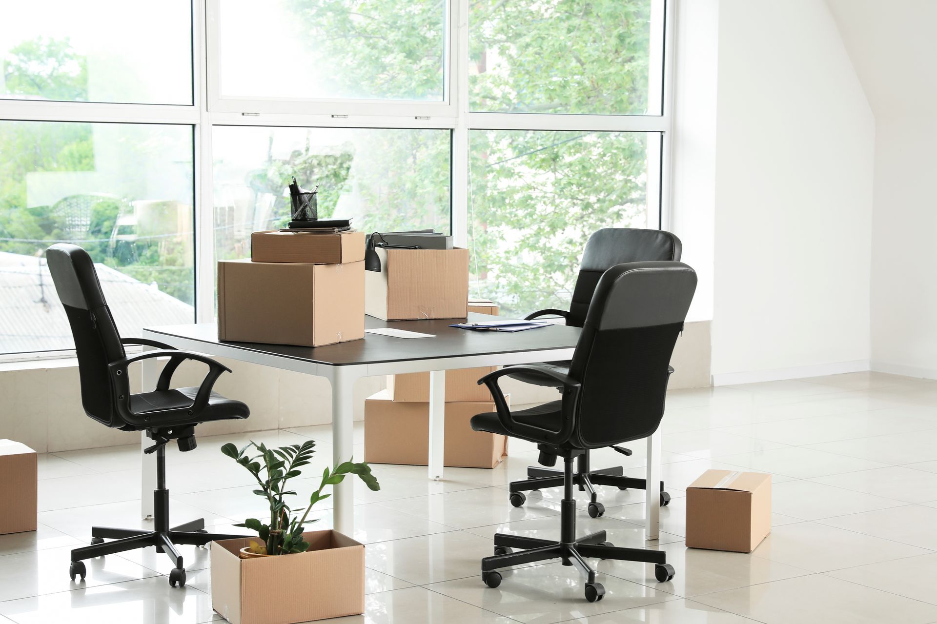 Bureau vide avec deux chaises noires, des cartons de déménagement et un bureau près de grandes fenêtres