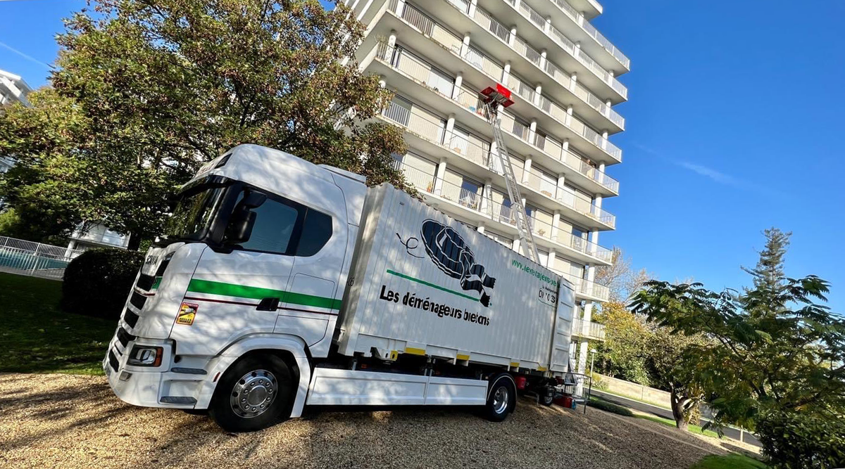 Camion de livraison blanc garé à côté d'un grand immeuble d'appartements par une journée ensoleillée.