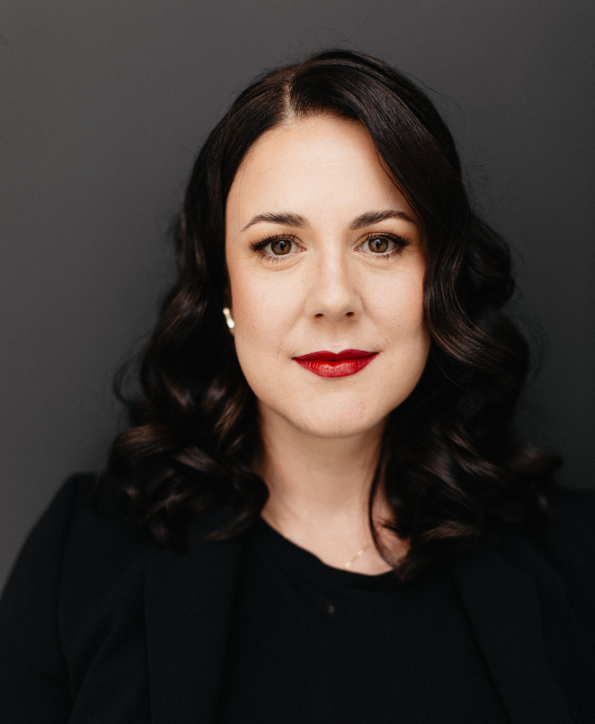 Frau mit dunklen Haaren und rotem Lippenstift blickt in Kamera