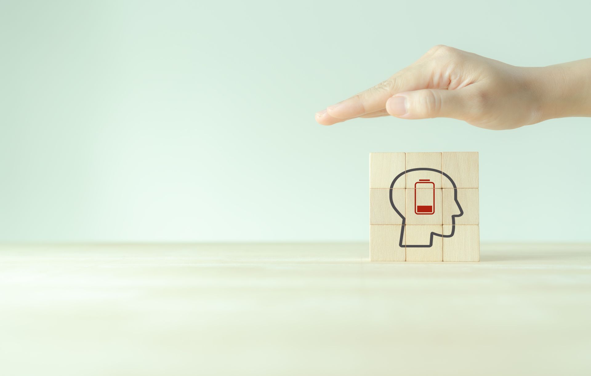 Eine Hand hält einen Holzblock, auf dem ein Kopf aufgemalt ist.