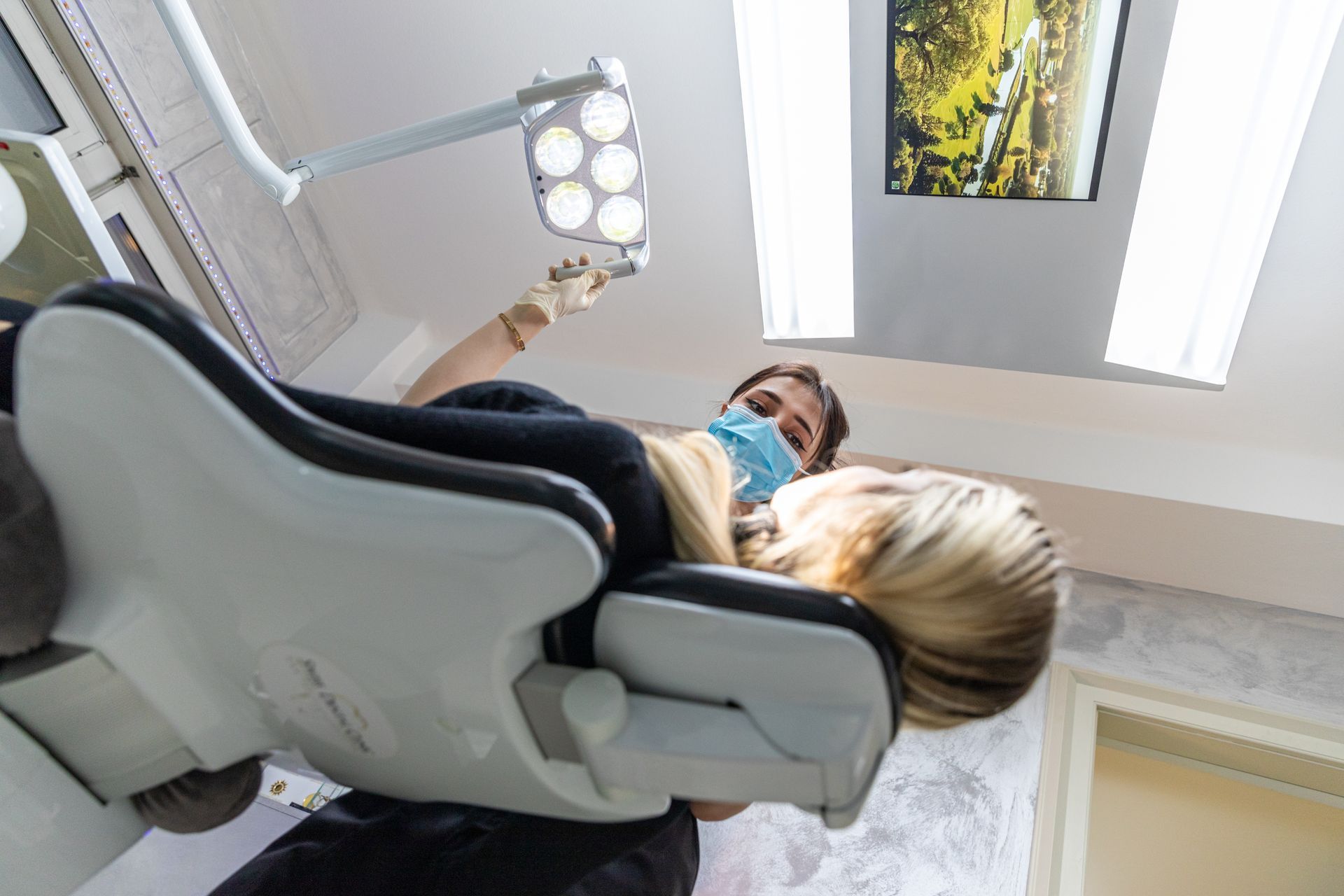 Dentista con mascherina che regola la luce sopra il paziente reclinato sulla poltrona del dentista.